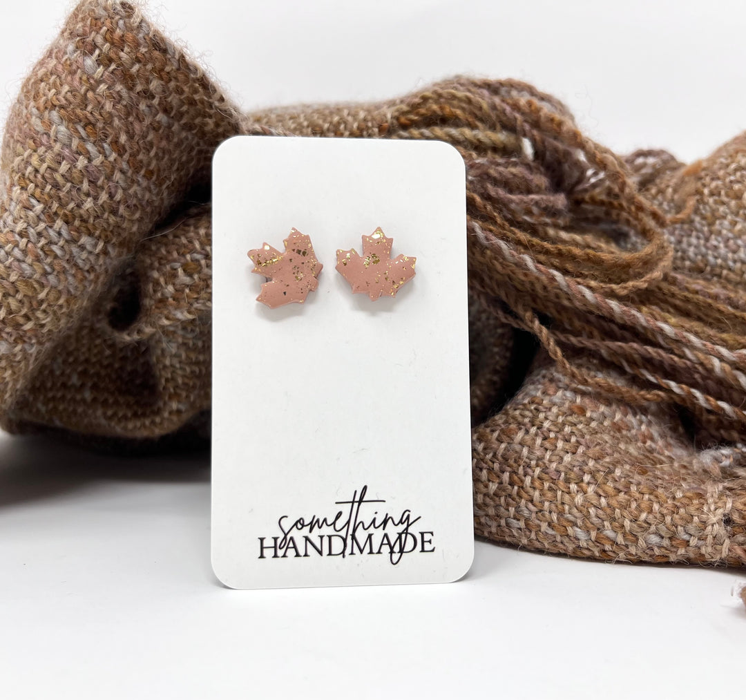 Pink and gold maple leaf stud earrings on a &